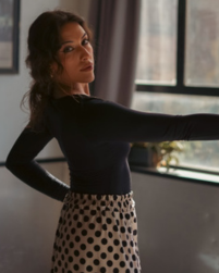 Photo of Marian Gonzalez, a female flamenco dancer in a black dress with her right arm raised to near the top of her head. 