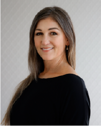 Two women in black tops and grey skirts dancing together with a long braid between them connecting each to the other. They lean away from one another.