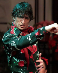 Two women in black tops and grey skirts dancing together with a long braid between them connecting each to the other. They lean away from one another.