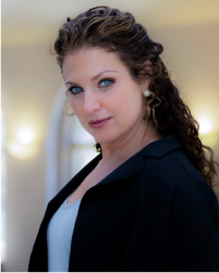 Two women in black tops and grey skirts dancing together with a long braid between them connecting each to the other. They lean away from one another.