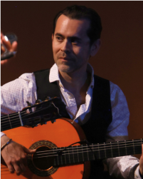 Two women in black tops and grey skirts dancing together with a long braid between them connecting each to the other. They lean away from one another.