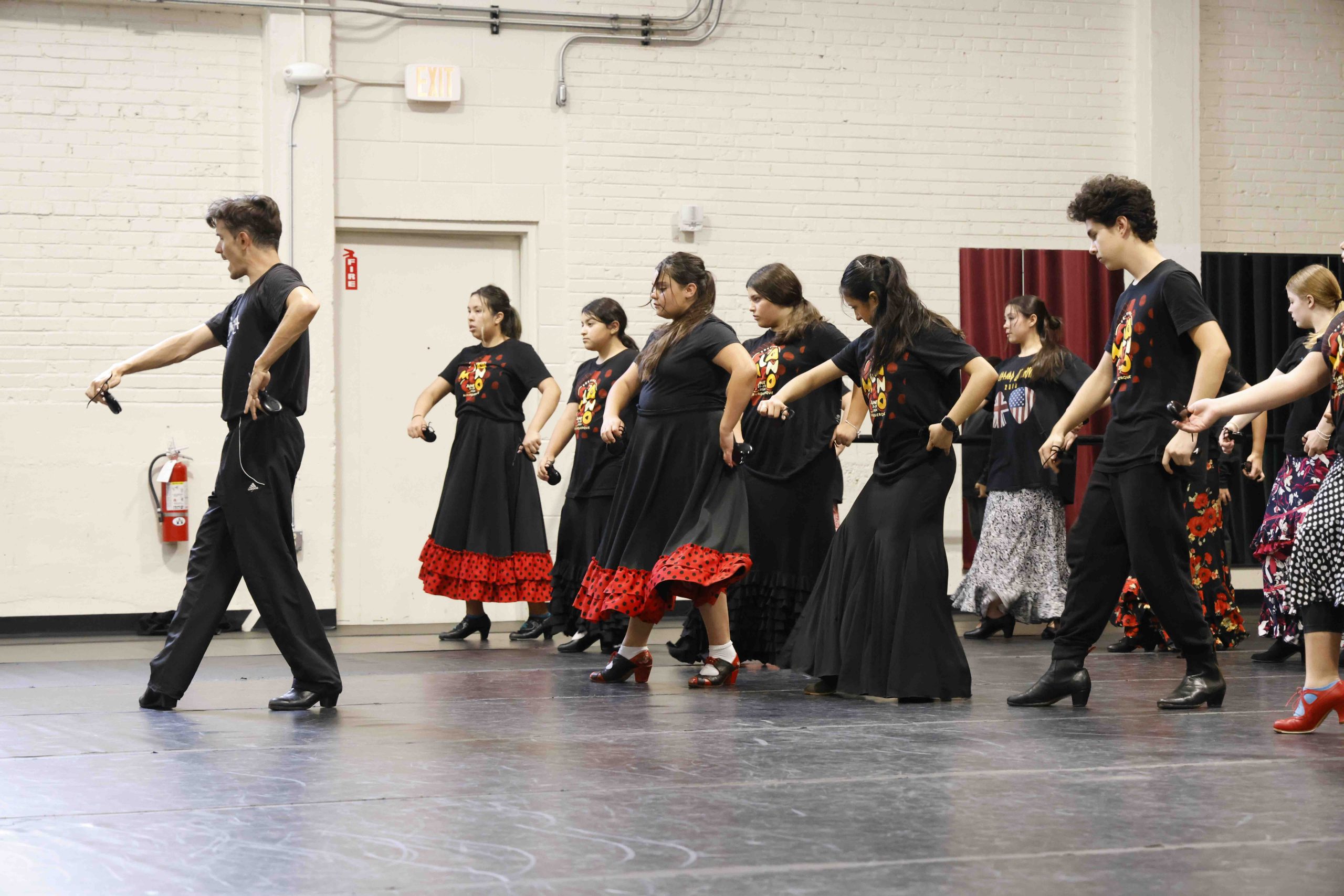 Un bailarín imparte una clase a un grupo de jóvenes alumnos. Visten de negro y tocan las castañuelas. 